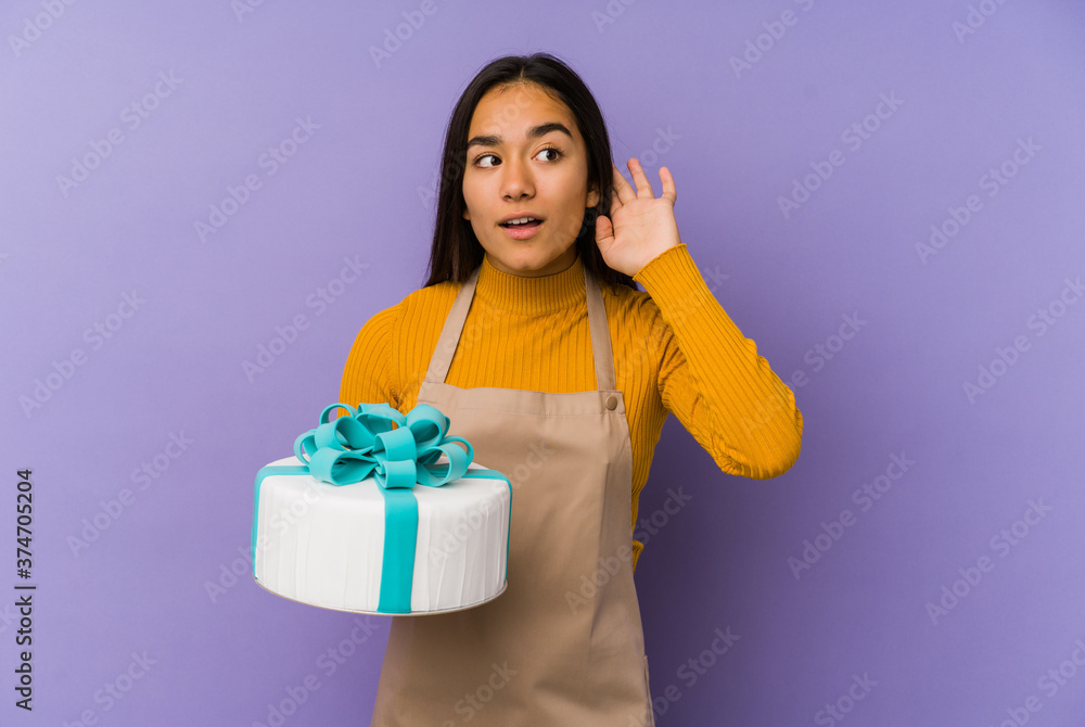 Young asian woman holding a cake isolated trying to listening a gossip. Young asian woman holding a cake isolated trying to listening a gossip.