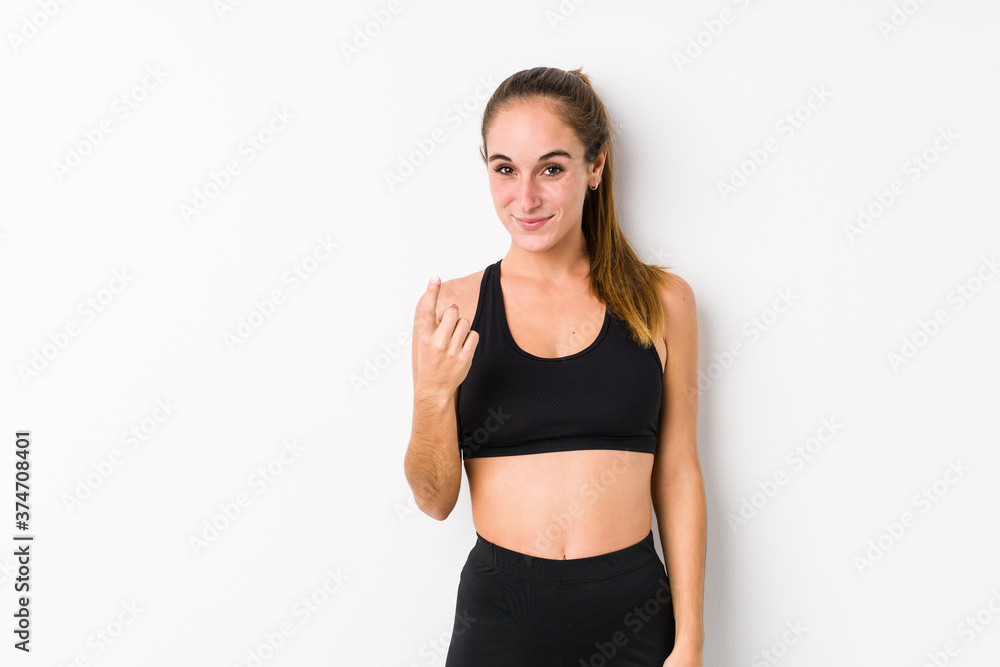 Young caucasian fitness woman posing in a white background pointing with finger at you as if inviting come closer. Young caucasian fitness woman posing in a white background pointing with finger at you as if inviting come closer.