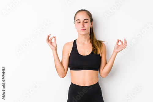 Young caucasian fitness woman posing in a white background relaxes after hard working day, she is performing yoga.