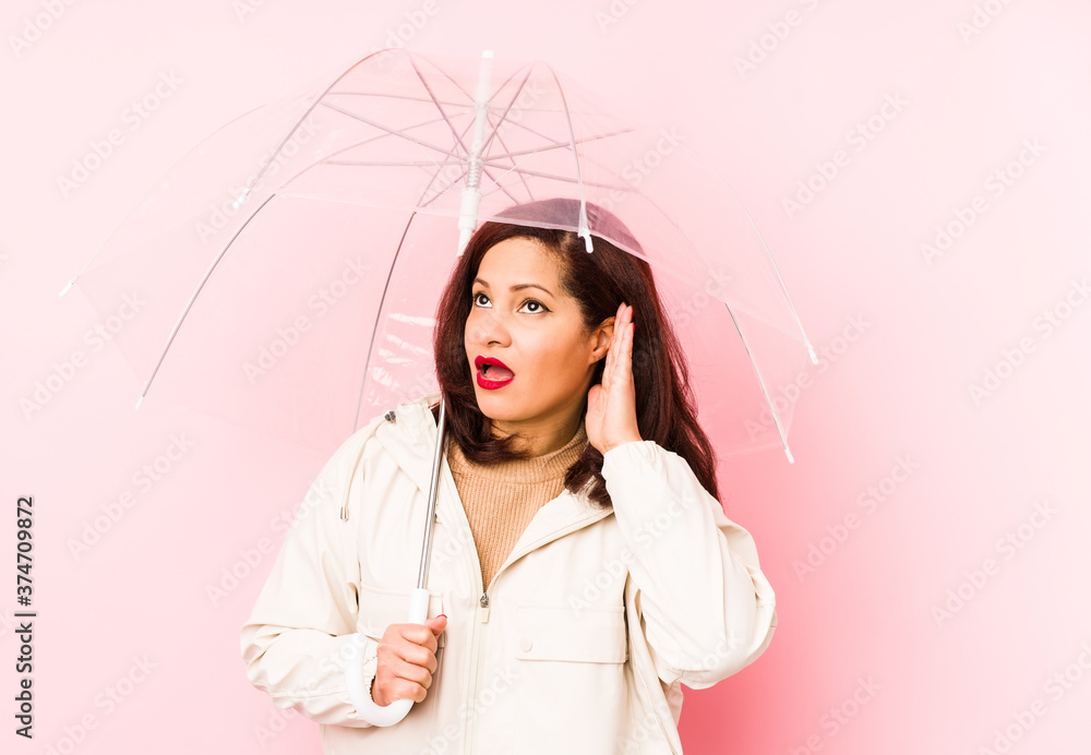 Fototapeta premium Middle age latin woman wearing an umbrella isolated trying to listening a gossip.