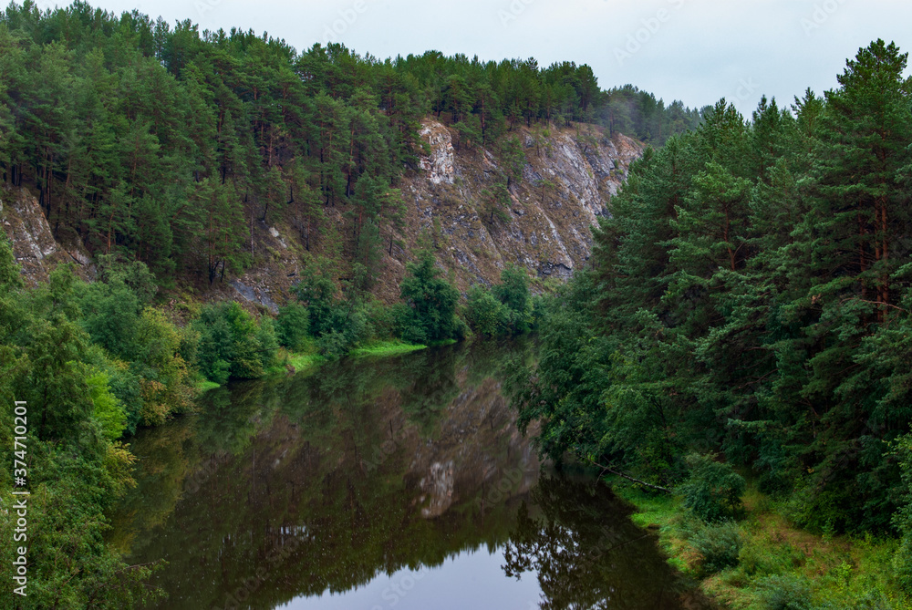 Fototapeta premium Beautiful river landscape with wooded mountain slopes. Limestone rocks in the Ural mountains. Cloudy sky in the background. Natural monument 