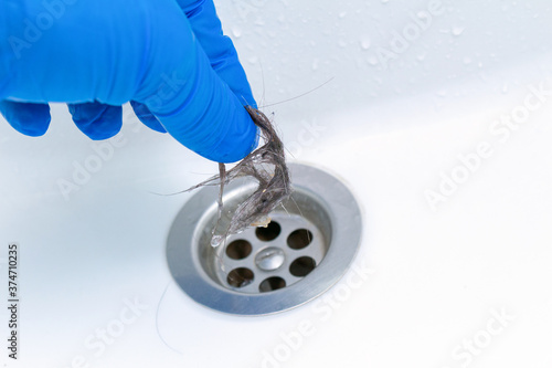 hand in glove cleaning a clogged sink or bathtub drain from hair