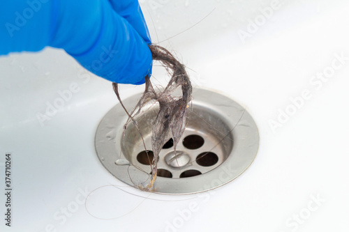 hand in glove cleaning a clogged sink or bathtub drain from hair
