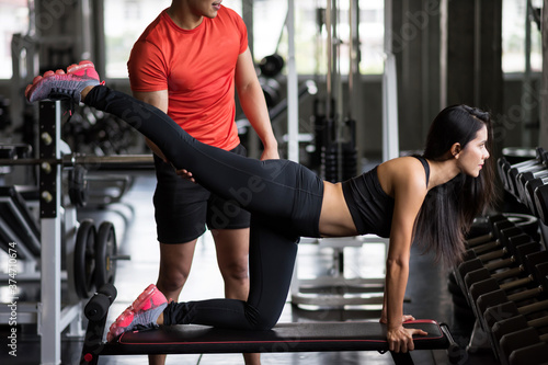 Personal trainer help Asian girl to stretch leg in gym