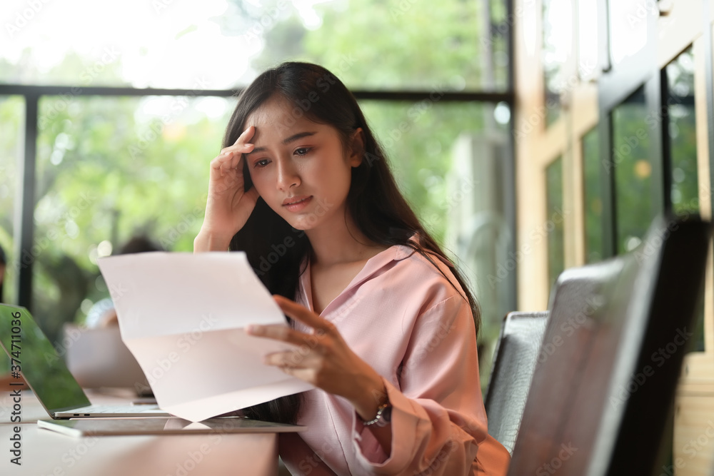 A stressed woman is keeping hands on the head while reading paperwork in the meeting room. A stressed woman is keeping hands on the head while reading paperwork in the meeting room.