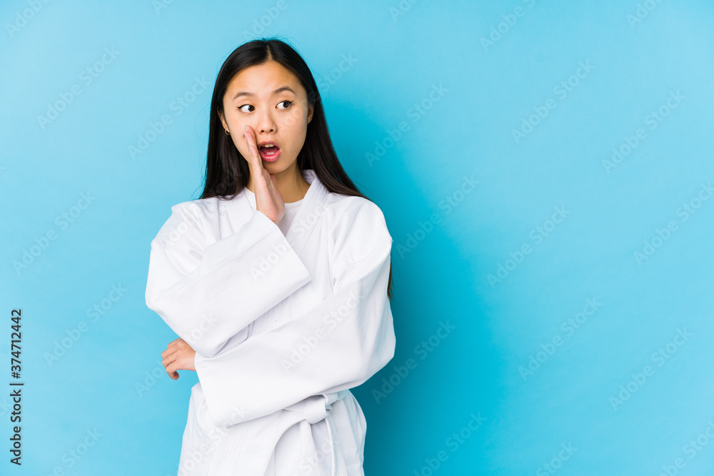 Young chinese woman practicing karate isolated is saying a secret hot braking news and looking aside Young chinese woman practicing karate isolated is saying a secret hot braking news and looking aside