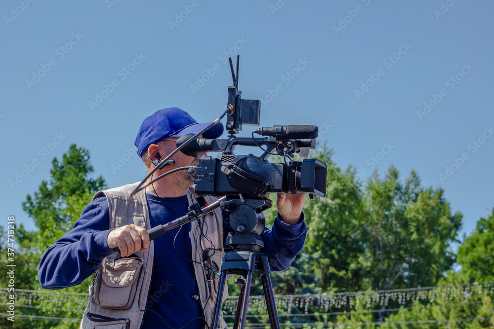 Cameraman with a movie camera against the background of a green forest and blue sky. The operator shoots a movie. Cameraman with a movie camera against the background of a green forest and blue sky. The operator shoots a movie.