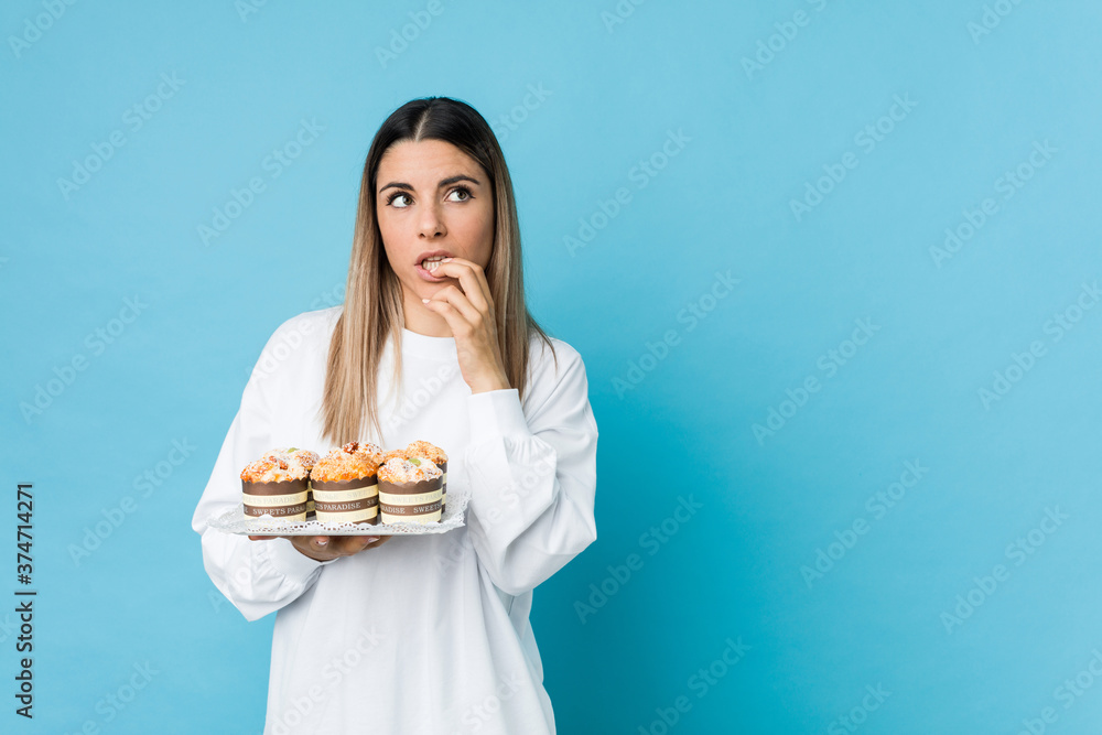 Young caucasian woman holding a sweets cake relaxed thinking about something looking at a copy space.