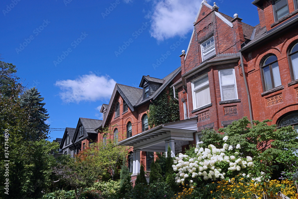 Street of old semi-detached houses with gables and summer flowers in lush gardens