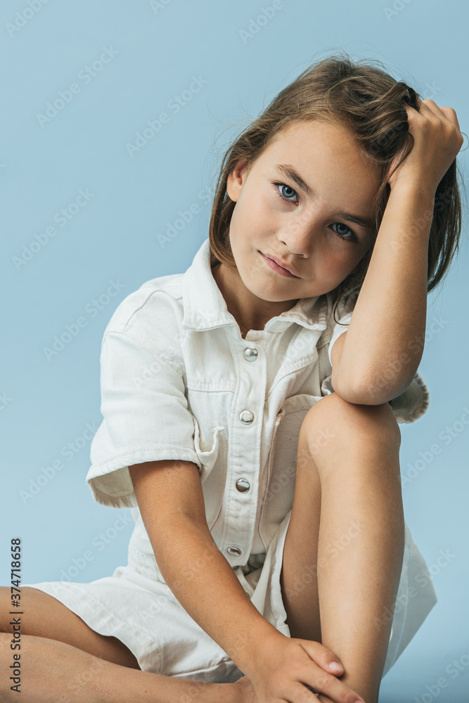 Serious little girl in a white thick romper suit sitting on the floor