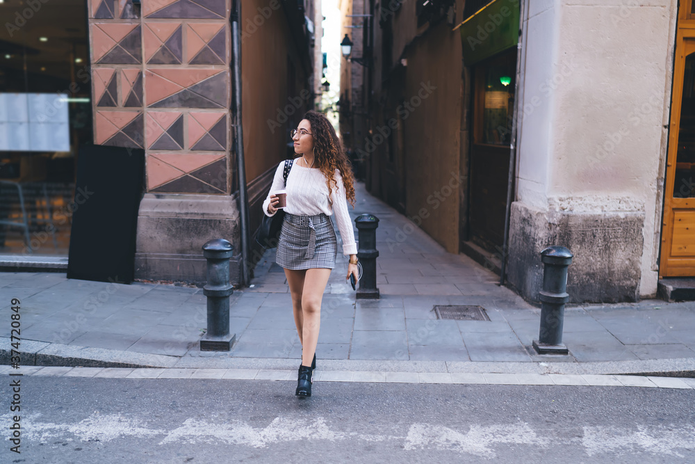 Trendy concentrated woman crossing street with cup of coffee
