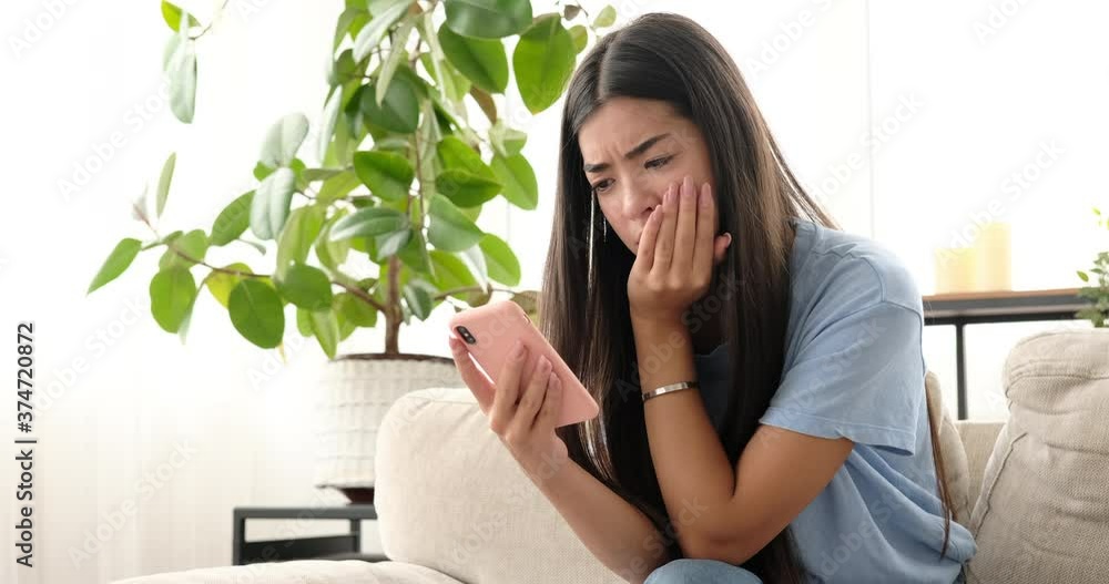 Woman shocked and displeased using mobile phone at home Woman shocked and displeased using mobile phone at home