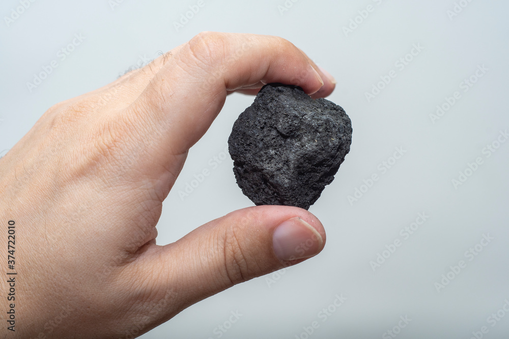 Male hand with a small piece of coal on a light background. An image on the theme of geology and the extraction of minerals and natural fuels. Male hand with a small piece of coal on a light background. An image on the theme of geology and the extraction of minerals and natural fuels.