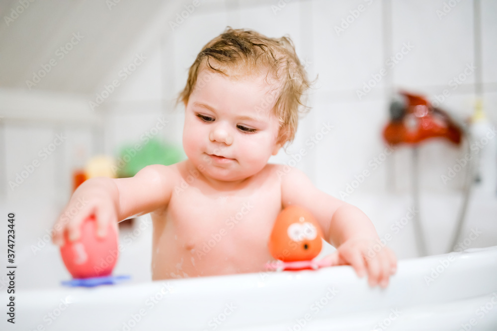 Cute adorable baby girl taking foamy bath in bathtub. Toddler playing with bath rubber toys. Beautiful child having fun with colorful gum toys and foam bubbles Cute adorable baby girl taking foamy bath in bathtub. Toddler playing with bath rubber toys. Beautiful child having fun with colorful gum toys and foam bubbles