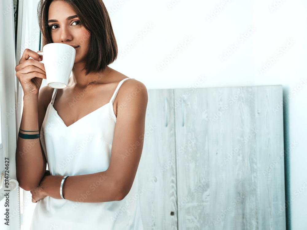 Portrait of beautiful woman dressed in white pajamas. Carefree female holds cup and drinking coffee. Sexy model enjoying her morning breakfast at balcony Portrait of beautiful woman dressed in white pajamas. Carefree female holds cup and drinking coffee. Sexy model enjoying her morning breakfast at balcony