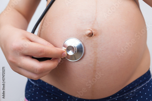 Pregnant woman with a stethoscope listens to her baby's heartbeat