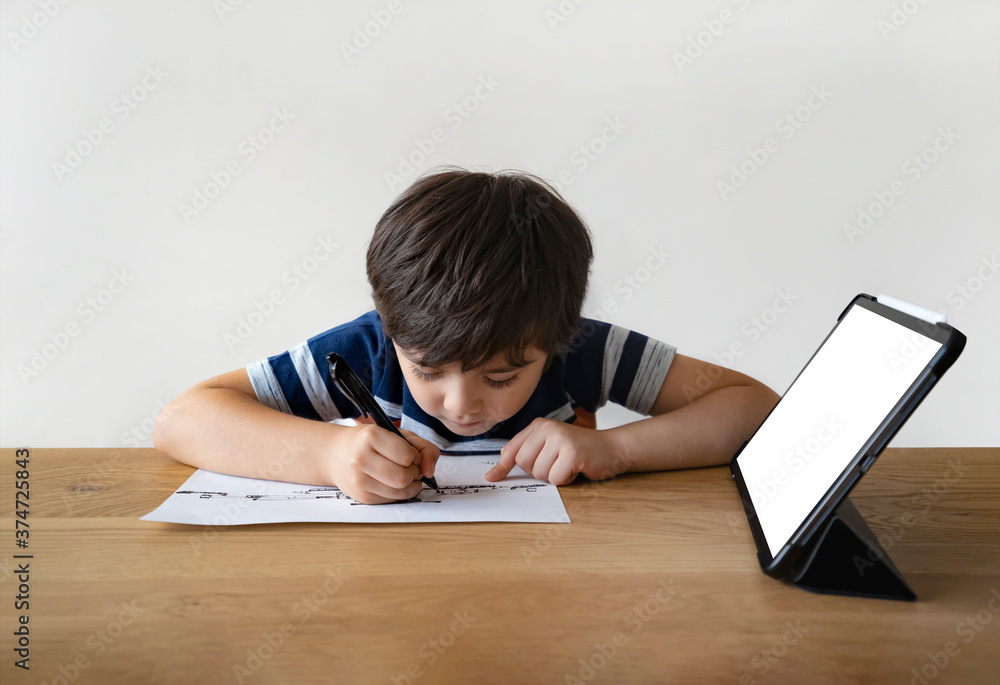 School Kid using pen drawing on paper, A boy doing home work sitting with mock up tablet, Child using digital pad searching information on internet for his study at home, E-learning online education School Kid using pen drawing on paper, A boy doing home work sitting with mock up tablet, Child using digital pad searching information on internet for his study at home, E-learning online education