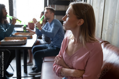 Upset offended young woman sitting separately, apart from diverse friends in cafe close up, sad excluded female feeling outsider, bad friendship concept, problem with communication, social outcast photo