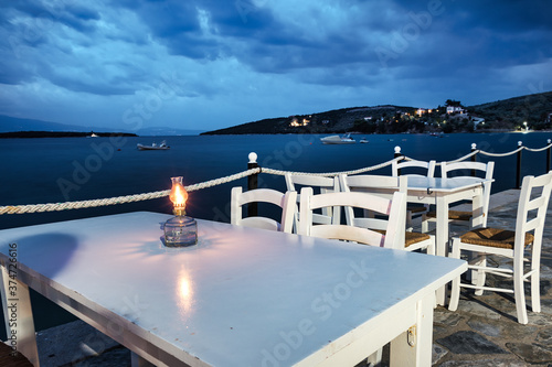 Traditional white wooden tables and chairs of a greek tavern at night and the view of the beach of Amaliapoli, Greece. photo