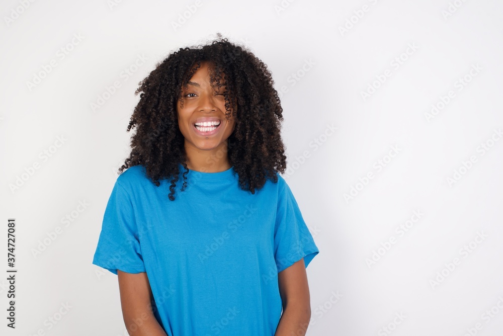 Shot of positive coquettish Young african woman with curly hair wearing casual smiling happily, blinking at camera in a playful manner, flirting with you. Human facial expressions and emotions Shot of positive coquettish Young african woman with curly hair wearing casual smiling happily, blinking at camera in a playful manner, flirting with you. Human facial expressions and emotions