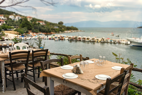 Traditional wooden tables and chairs of a greek tavern over the view of the port of Amaliapoli, Greece.