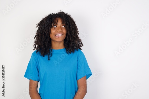 Photo of amazed Young african woman with curly hair wearing casual blue shirt over white background bitting lip and looking up to empty space,