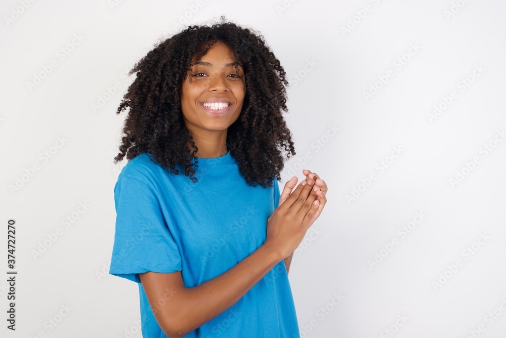 Young african woman with curly hair wearing casual blue shirt over white background clapping and applauding happy and joyful, smiling proud hands together. Young african woman with curly hair wearing casual blue shirt over white background clapping and applauding happy and joyful, smiling proud hands together.
