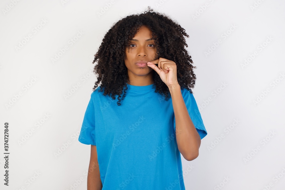 Young african woman with curly hair wearing casual blue shirt over white background mouth and lips shut as zip with fingers. Secret and silent, taboo talking. Young african woman with curly hair wearing casual blue shirt over white background mouth and lips shut as zip with fingers. Secret and silent, taboo talking.