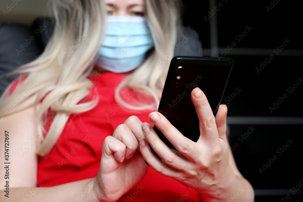 Blonde woman in face mask using smartphone, mobile phone in female hands closeup. Concept of safety work in office during coronavirus pandemic