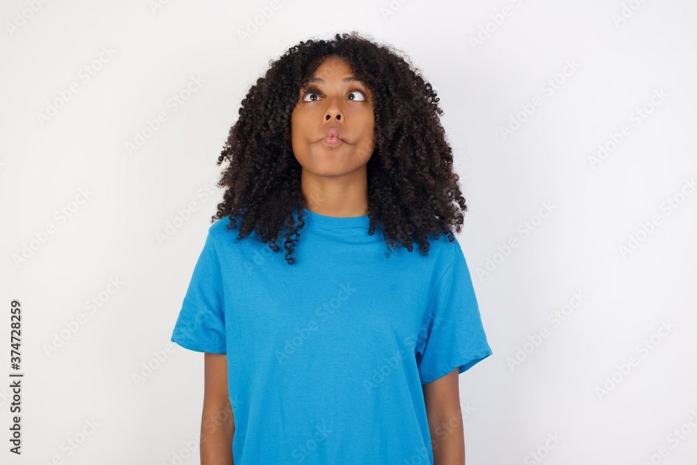 Young african woman with curly hair wearing casual blue shirt over white background making fish face with lips, crazy and comical gesture. Funny expression. Young african woman with curly hair wearing casual blue shirt over white background making fish face with lips, crazy and comical gesture. Funny expression.
