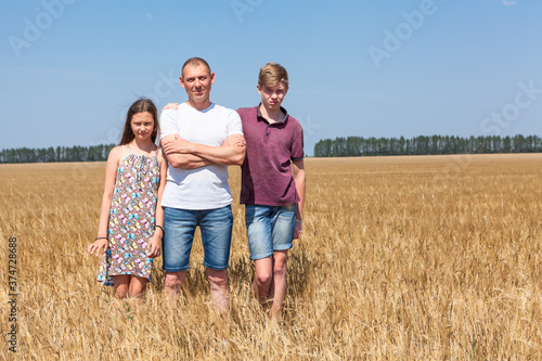 Single father with two kids standing on wheat field at summer, copy space, three people family portrait, copyspace