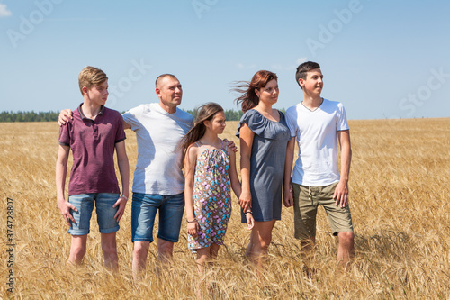 Large family from father, mother, two brothers and sister standing in line on wheat field, full length portrait