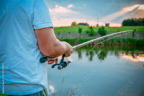 Young man fishing on lake at sunset enjoying hobby. Outdoor, activity. Narrow focus.