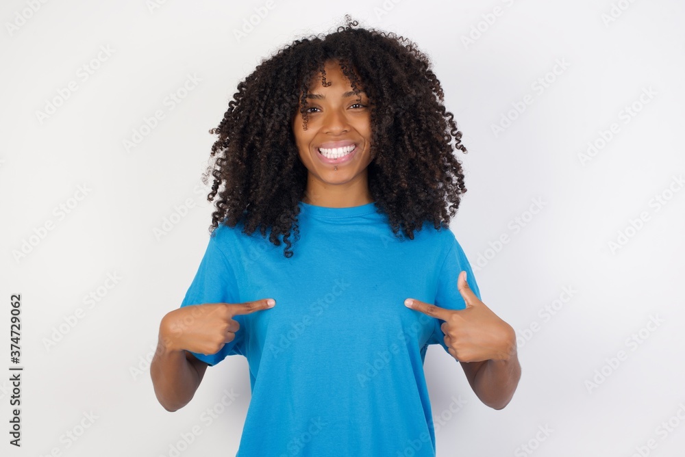 Horizontal shot of cheerful Young african woman with curly hair wearing casual blue shirt points at his body, being in good mood after going shopping and making successful purchases Horizontal shot of cheerful Young african woman with curly hair wearing casual blue shirt points at his body, being in good mood after going shopping and making successful purchases