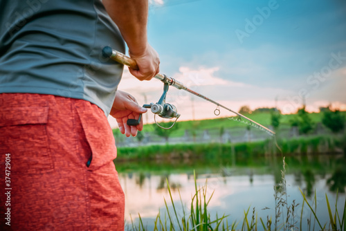 Young man fishing on lake at sunset enjoying hobby. Outdoor, activity. Narrow focus.