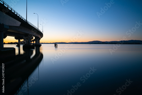 Curving lines and calm water by Tauranga Harbour Bridge and colour in the sky at sunrise