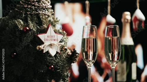 Close up of two glasses of champagne with bubbles. Romantic dinner. A decorated Christmas tree stands nearby. A fireplace burns in the background.