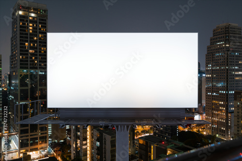 Blank white road billboard with Bangkok cityscape background at night time. Street advertising poster, mock up, 3D rendering. Front view. The concept of marketing communication to promote idea.