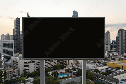 Blank black road billboard with Bangkok cityscape background at sunset. Street advertising poster, mock up, 3D rendering. Front view. The concept of marketing communication to promote or sell idea.