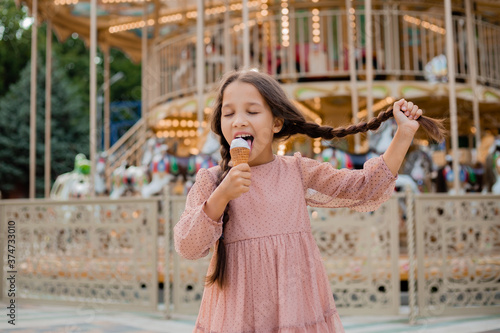Teenage brunette girl holds on to pigtail and eats ice cream at the park