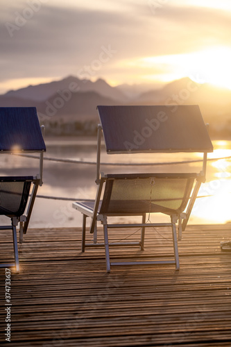 Two empty chairs on a wooden pier at sunset