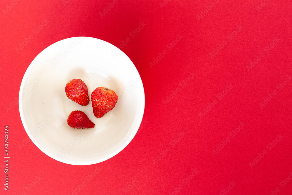 three red strawberries on a white plate on the red background, isolated three red strawberries on a white plate on the red background, isolated