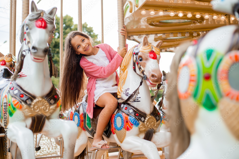 A teenage girl with long hair rolls around on a swing horse carousel. Sitting on a horse at an amusement park