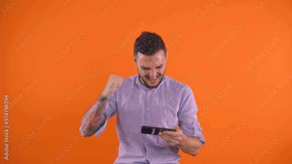 tatooed beared man screaming and rejoicing win of football team while watching game on smartphone ,betting concepts isolated mandarin color background tatooed beared man screaming and rejoicing win of football team while watching game on smartphone ,betting concepts isolated mandarin color background
