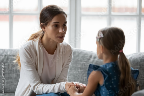 Worried young mommy holding hands of unhappy little child daughter, supporting in hard life situation, giving advice against bullying, soothing comforting or apologizing after quarrel at home.