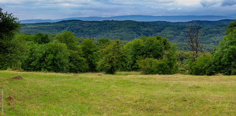 Foothill landscape, meadow with mown grass on a warm summer day with a panorama of mountains on the horizon. Foothill landscape, meadow with mown grass on a warm summer day with a panorama of mountains on the horizon.