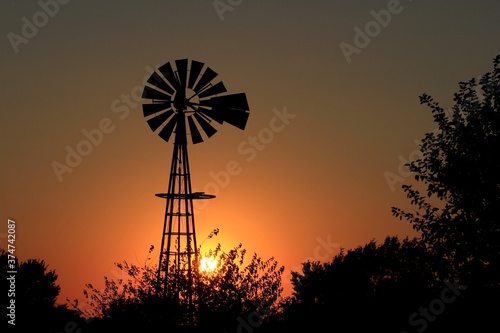 Kansas Sunset with a Windmill silhouette and tree's with a colorful sky.