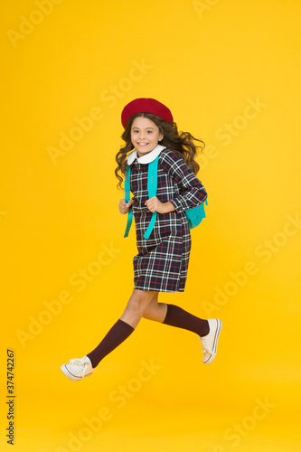 stylish teen college student jumping. little girl with backpack going to school. education concept. school and fashion. child in pupil uniform. kid in french beret on yellow background. hurry up