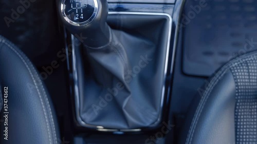 The driver's hand takes a shiny black lever and engages the reverse gear in the manual transmission and presses the metal button of the anti-theft system to lock the lever and then unlocks the system  photo