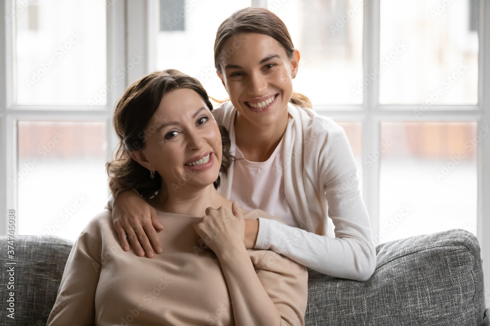 Φωτογραφία Portrait of smiling millennial woman cuddling happy beautiful middle aged mother sitting on sofa